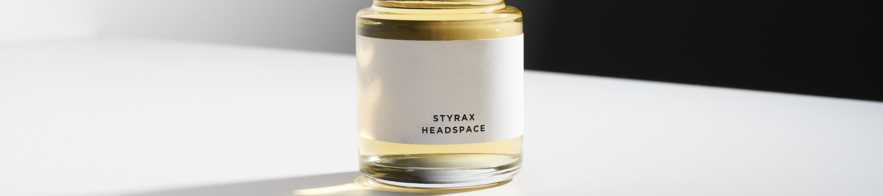 Bottle of Styrax Headspace perfume placed on a bright white surface, brand presentation banner for HEADSPACE