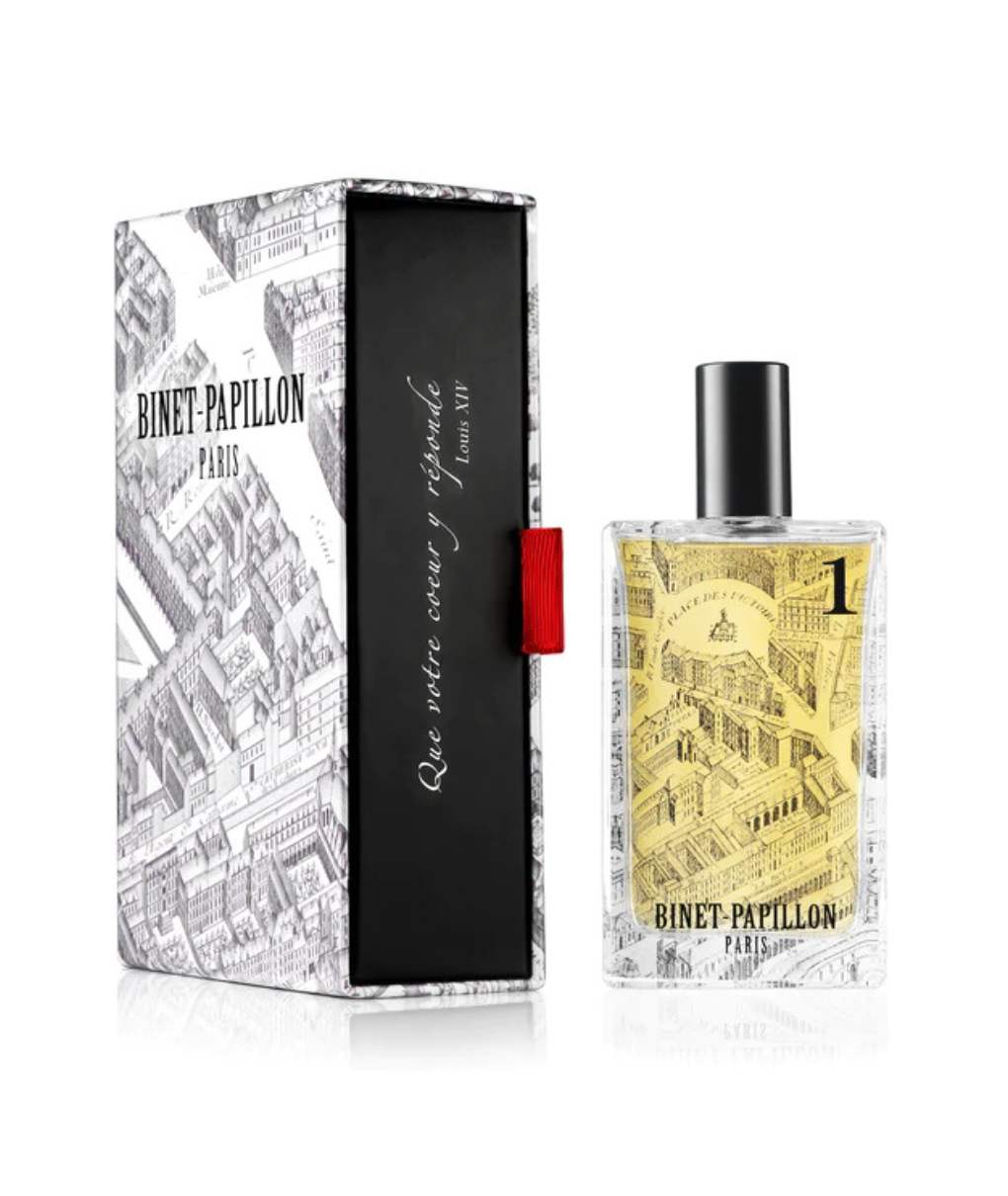 L'image montre un flacon de parfum placé à côté d’un coffret. Le flacon est rectangulaire et transparent, avec un bouchon noir. Le décor représente un motif en noir et blanc, représentant des scènes architecturales, ce qui donne un aspect artistique et vintage. À l'intérieur, le parfum a une teinte dorée. Le coffret est décoré avec des illustrations similaires à celles du flacon. Il est principalement blanc avec des détails en noir. On peut lire "BINET-PAPILLON" en bas de la boîte, avec une inscription en rouge à côté.