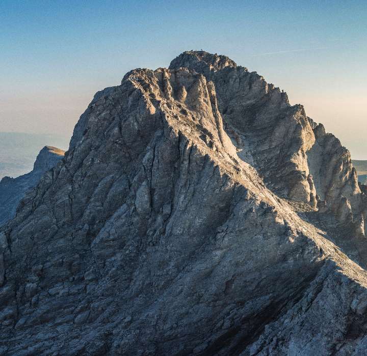 Een steile bergtop onder een heldere lucht, met rotsachtige hellingen en uitgesproken schaduwen.