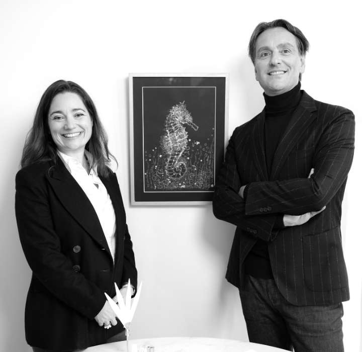 Une femme souriante et un homme dans un costume, posent ensemble devant une œuvre d'art représentant un hippocampe, sur un fond clair.