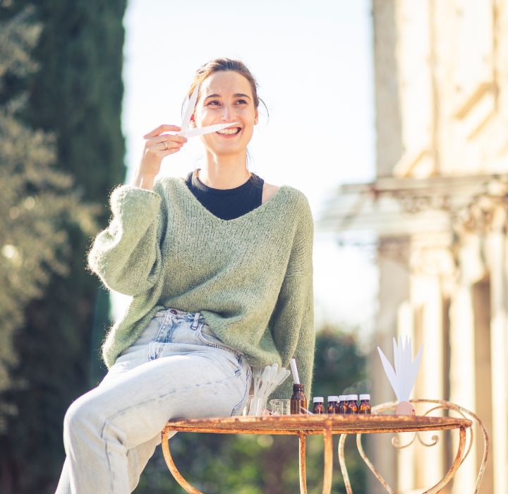 Femme souriante sentant un bâtonnet olfactif, découverte de parfums niche CÉPAGES PARFUMS en plein air