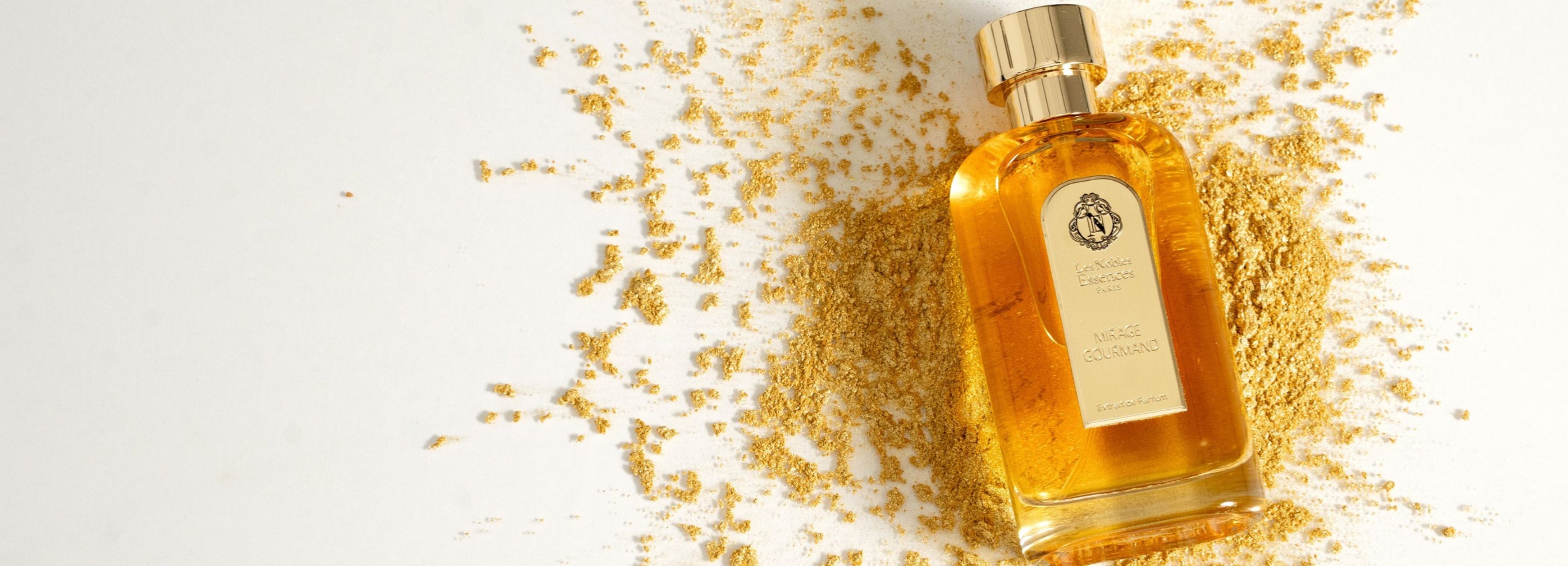 Un flacon de parfum "Mirage Gourmand" posé sur un lit de poudre d'amande