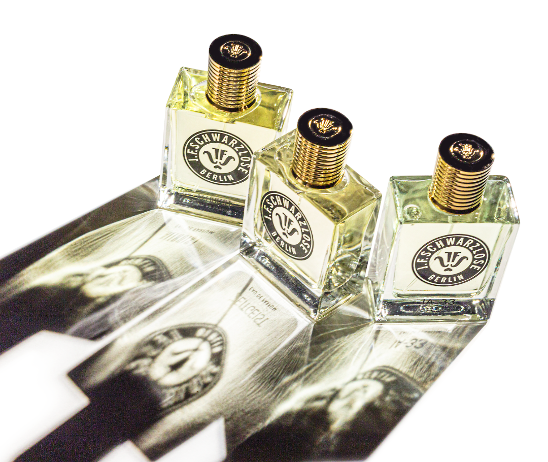 3 flaconi di profumo J.F. Schwarzlose visti dall’alto. Sono illuminati in modo tale che la loro ombra duplichi i flaconi e li proietti sul pavimento chiaro.