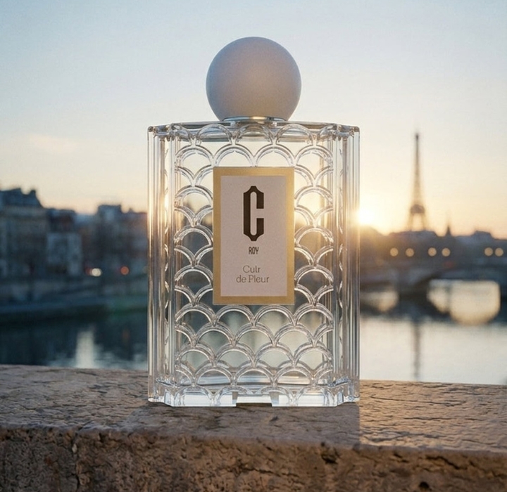 A bottle of C_Ray perfume is placed on a bridge in Paris at sunset. In the background, the Eiffel Tower.