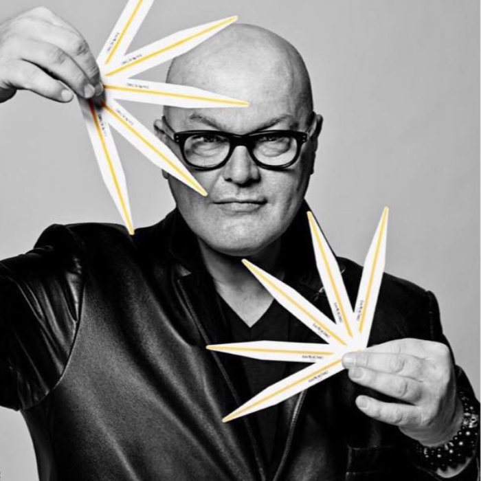 Perfumer Jean Michel Duriez is dressed in a black shirt. He is holding scent strips in both hands, as if he were holding fans.