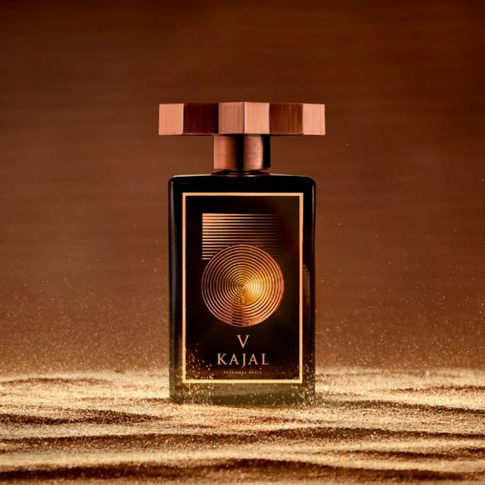 Un flacon de parfum cuivre et or, posé sur du sable en mouvement