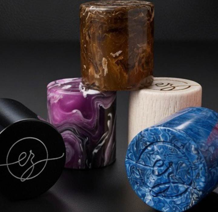 Primer plano de los tapones artesanales de Claudio Zucca Parfums con texturas marmoleadas, de madera y coloridas, grabados con el logotipo cz.