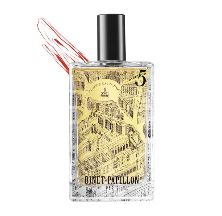 Ce flacon est rectangulaire avec un bouchon noir, l'étiquette présente une illustration en noir et blanc d'une vue de la ville, probablement une scène architecturale. Le fond est coloré en jaune, et il y a une touche de rouge qui attire l'attention. Le nom