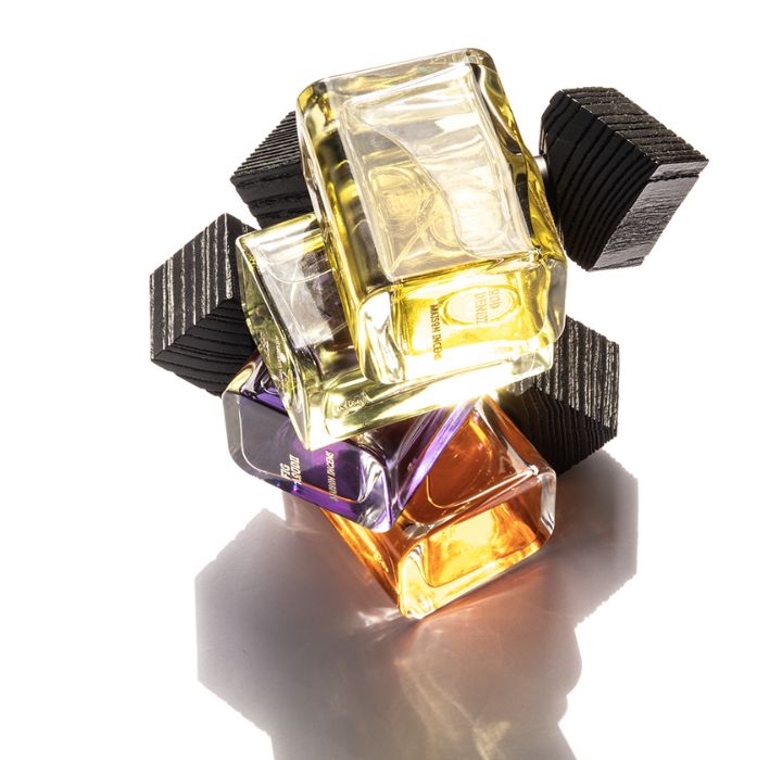 La photo présente trois flacons de parfum luxueux de la marque de parfum de niche MAISON INCENS, contenant un liquide doré. Les bouteilles sont placées en diagonale sur une surface réfléchissante, en partant du bas à gauche et en se déplaçant vers le haut à droite. Le flacon au premier plan est clairement étiqueté « SANTAL TISLIT » et « MAISON INCENS », avec un bouchon métallique ajoutant à son aspect sophistiqué. La deuxième bouteille est partiellement cachée par la première, tandis que la troisième bouteille n’est visible que de l’arrière, créant un arrangement intrigant. La marque MAISON INCENS est vendue sur la boutique en ligne SCENTISSIME.