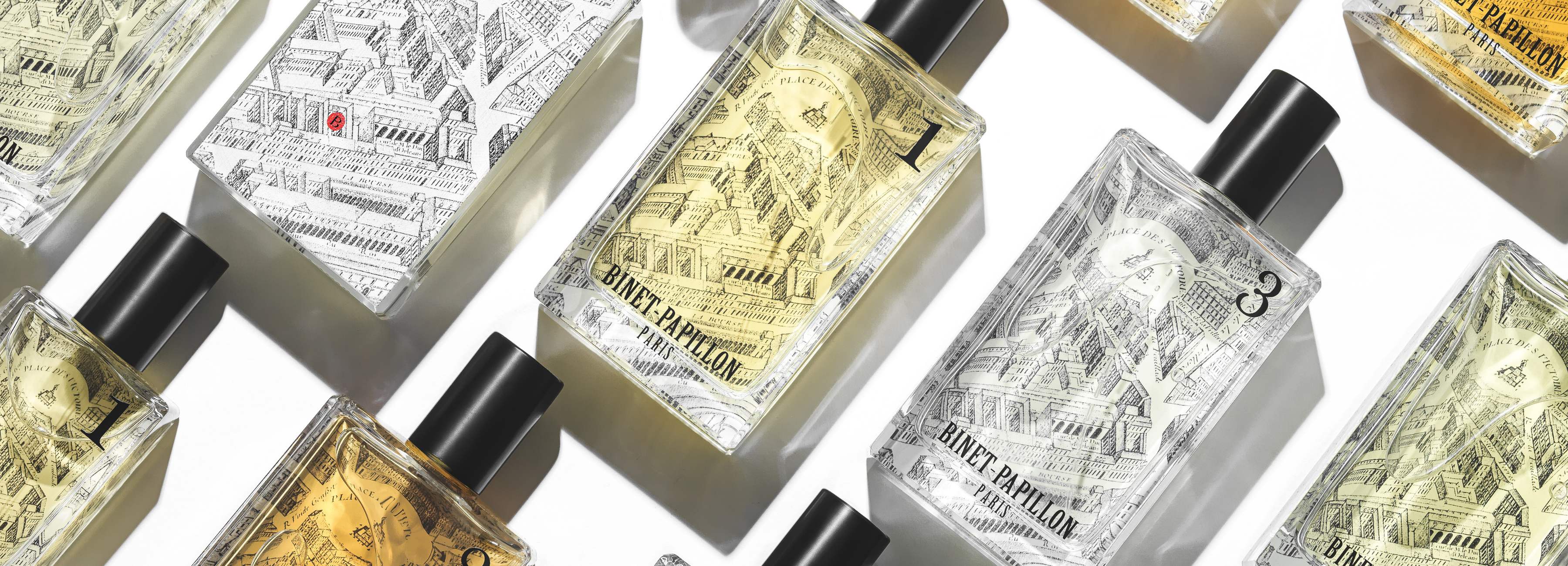 The image shows an arrangement of several perfume bottles from the niche perfume brand Binet-Papillon. The bottles are rectangular in shape with black caps.The bottle labels are adorned with detailed artistic motifs, depicting an old street map of a city, likely Paris, creating a vintage and elegant feel. The fragrances inside vary in color, from clear to golden yellow.The bottles are arranged in a sort of pattern, with some at a slight angle, creating an interesting visual dynamic. The lighting is bright and highlights the textures of the bottles and labels, adding a luxurious feel to the overall composition.