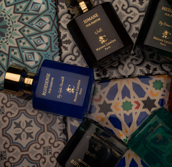 Plusieurs flacons de parfums Maison Cataliya bleu, noir et vert posés sur des carreaux de mosaïque zellige